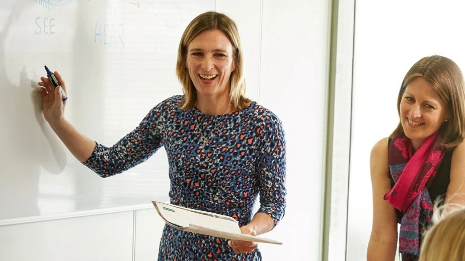 Women in meeting writing on whiteboard and laughing